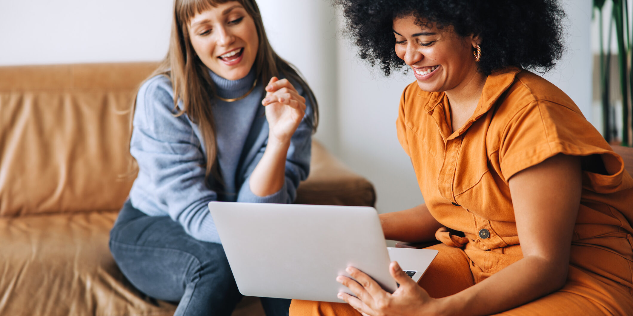 Discussing benefits. Cheerful young businesswomen smiling happily while using a laptop together. Two female entrepreneurs working as a team in a modern workplace.