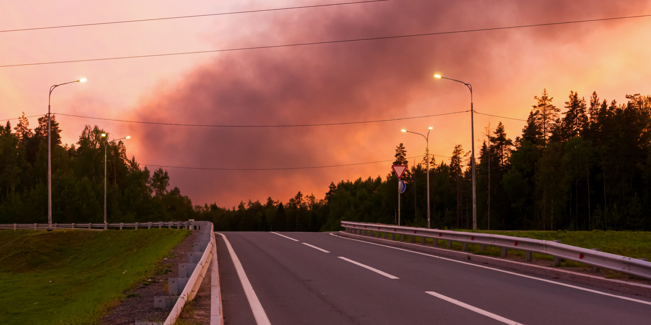 Black smoke from a fire in crimson sunset sky over the road in summer Black smoke from a fire in the crimson sky from the sunset over the road in summer