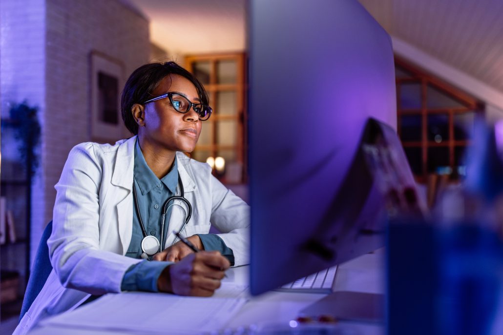 Young Female Doctor Late At Night Finishing Paper Work And Consulting Online With A Patient Using Computer In Her Office