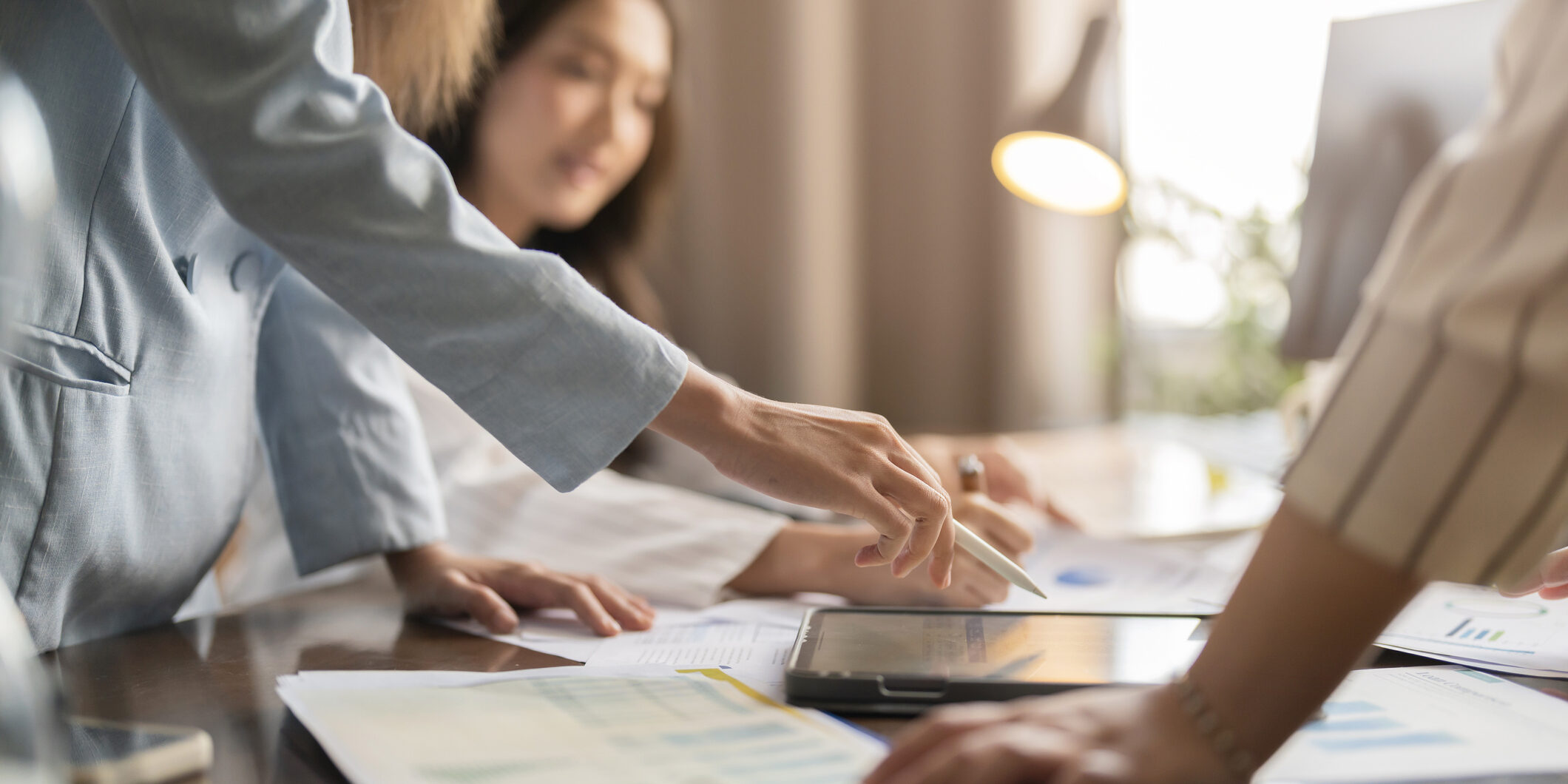 asian businesswoman brainstorm conference with her partners discussing about financial budget new project analysis with tablet and printed charts document in meeting room