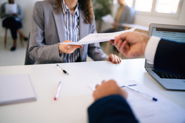 In the office young Caucasian female candidate, giving her CV or application form to male recruiter during a job interview